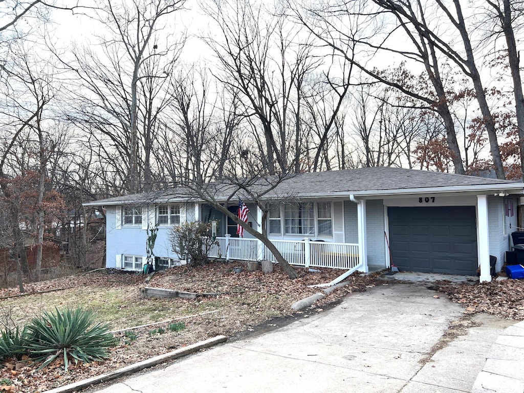 ranch-style home featuring a porch, a garage, brick siding, a shingled roof, and concrete driveway