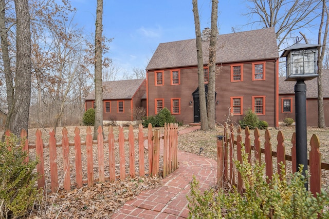 colonial home featuring a fenced front yard and a shingled roof