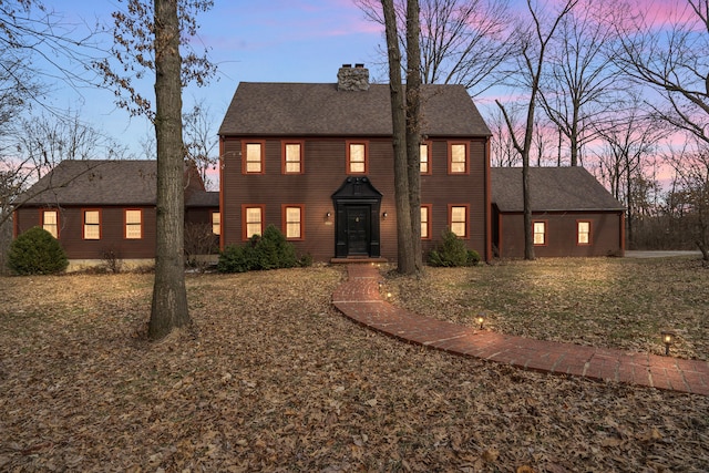 colonial-style house featuring a chimney and a shingled roof