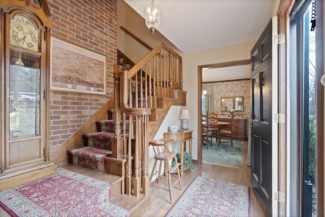 stairway with plenty of natural light, brick wall, wallpapered walls, and hardwood / wood-style floors