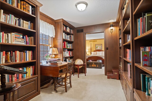 office space featuring light carpet, visible vents, crown molding, and wall of books