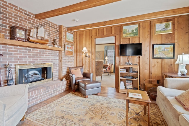 living area with beam ceiling, a brick fireplace, wood finished floors, and wood walls