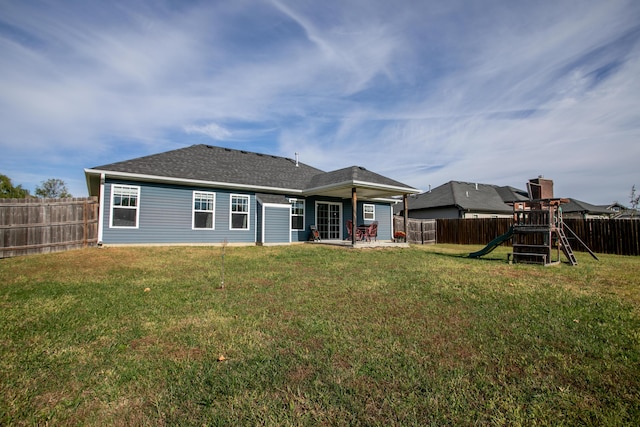 rear view of property featuring a playground, a yard, and a fenced backyard