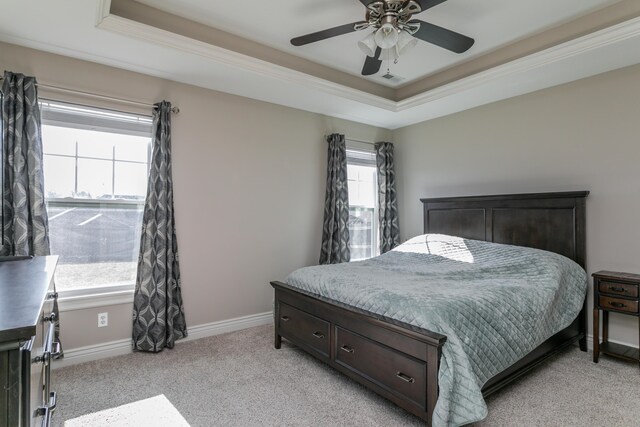 bedroom with light colored carpet, a raised ceiling, baseboards, and ceiling fan