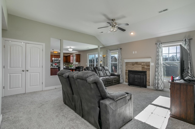 living area with visible vents, ceiling fan, light colored carpet, vaulted ceiling, and a stone fireplace