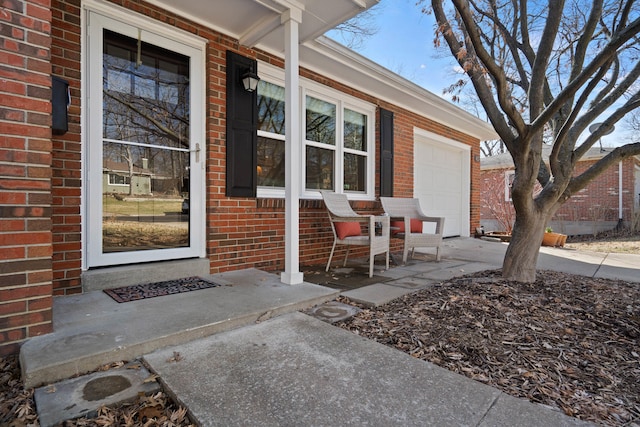 doorway to property featuring a garage, driveway, brick siding, and covered porch