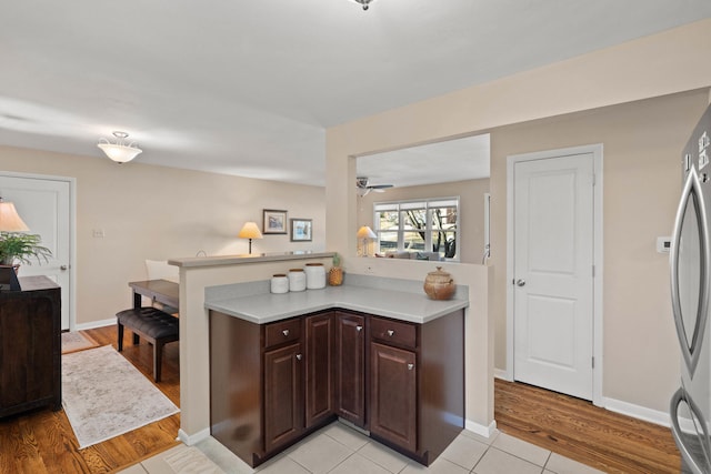 kitchen with light countertops, light wood-style flooring, a ceiling fan, freestanding refrigerator, and dark brown cabinetry