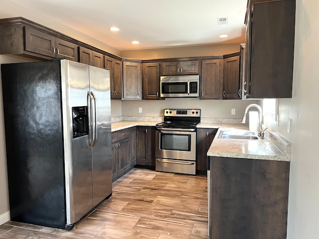 kitchen featuring visible vents, stainless steel appliances, dark brown cabinets, light countertops, and a sink