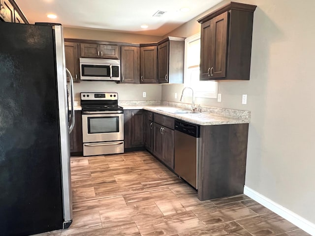 kitchen featuring light countertops, visible vents, appliances with stainless steel finishes, a sink, and dark brown cabinetry