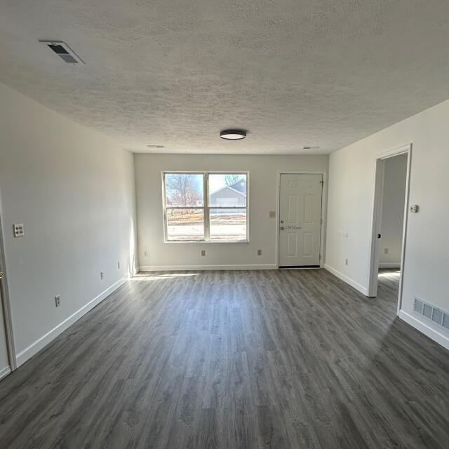 spare room with dark wood-type flooring, visible vents, a textured ceiling, and baseboards