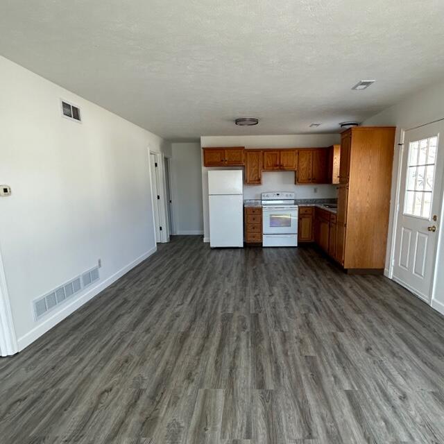 kitchen with white appliances, visible vents, brown cabinets, and dark wood-style flooring