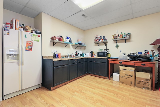 kitchen with light wood-style flooring, open shelves, white fridge with ice dispenser, light countertops, and a paneled ceiling