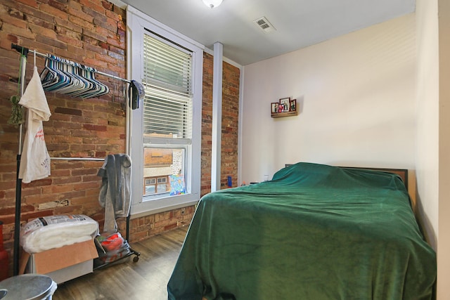 bedroom with visible vents, brick wall, and wood finished floors