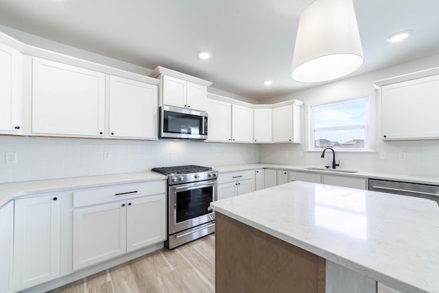 kitchen with a sink, stainless steel appliances, white cabinets, light wood finished floors, and decorative backsplash