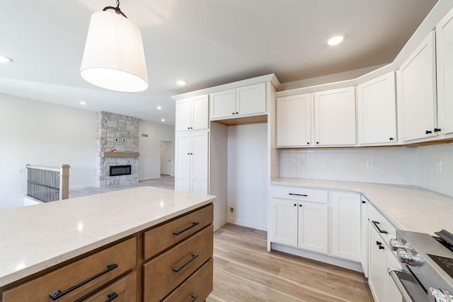 kitchen with light wood-type flooring, brown cabinets, stainless steel range oven, tasteful backsplash, and a fireplace