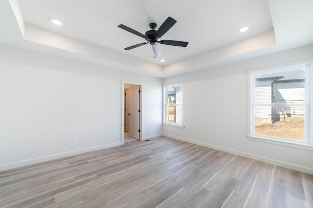 unfurnished room with recessed lighting, light wood-type flooring, a raised ceiling, and baseboards