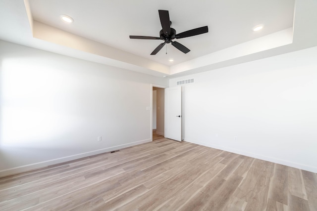 empty room featuring visible vents, a tray ceiling, recessed lighting, light wood finished floors, and baseboards