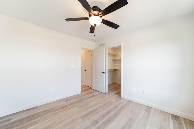 unfurnished bedroom with baseboards, ceiling fan, a spacious closet, light wood-style floors, and a closet