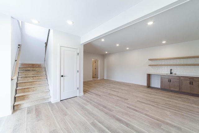 unfurnished living room with baseboards, light wood-style flooring, recessed lighting, a sink, and stairs