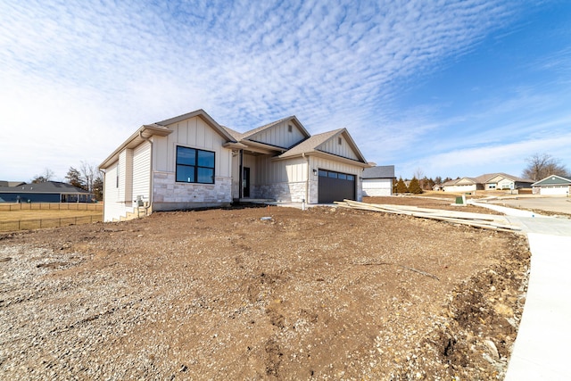 view of front of house with driveway, stone siding, fence, board and batten siding, and a garage