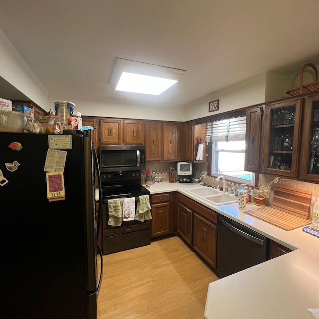 kitchen with a sink, stainless steel appliances, light countertops, glass insert cabinets, and light wood-style floors