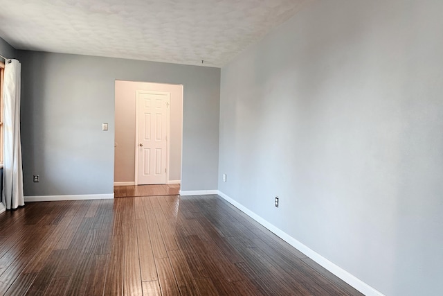 spare room featuring a textured ceiling, dark wood-type flooring, and baseboards