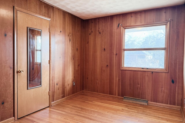 unfurnished room with visible vents, wood walls, and light wood-type flooring