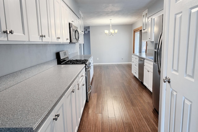 kitchen with baseboards, dark wood-style flooring, white cabinets, appliances with stainless steel finishes, and a notable chandelier