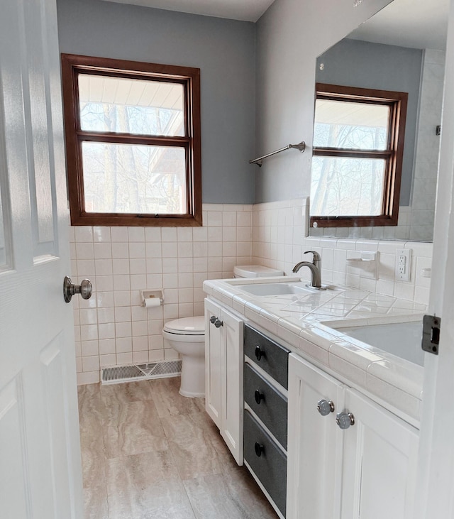 bathroom with visible vents, toilet, double vanity, tile walls, and a sink