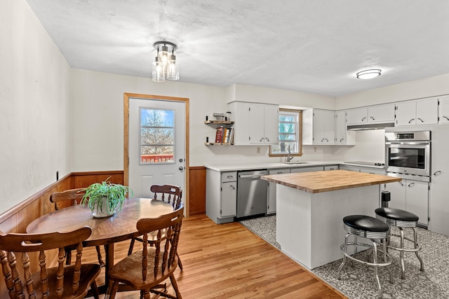 kitchen featuring wooden counters, light wood-style flooring, a sink, appliances with stainless steel finishes, and wainscoting