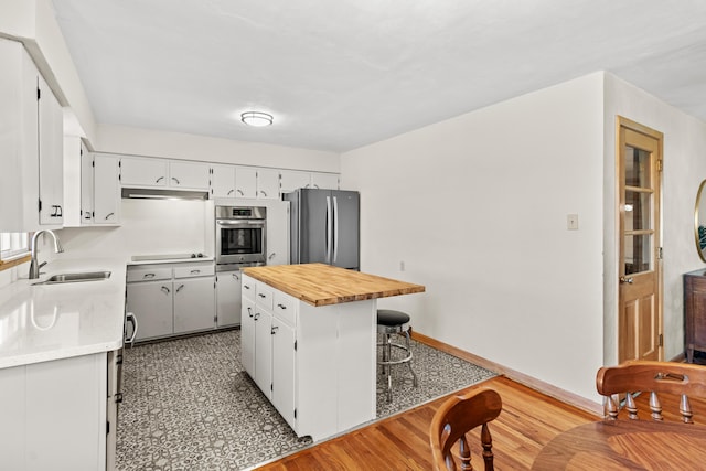 kitchen featuring a breakfast bar, a sink, appliances with stainless steel finishes, wood counters, and white cabinetry