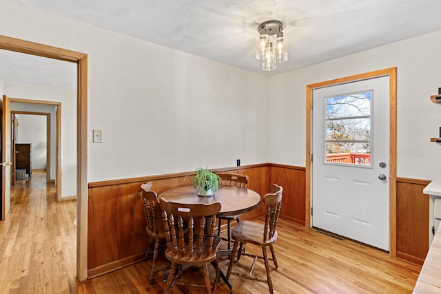 dining area with a wainscoted wall, wood walls, and light wood-type flooring