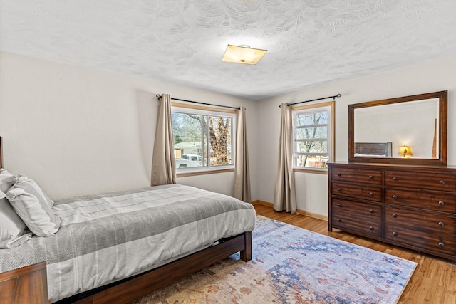 bedroom featuring baseboards, light wood-style floors, and a textured ceiling