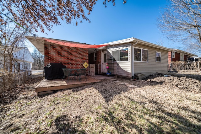 back of house with brick siding, a deck, and fence