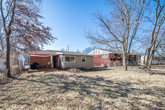 rear view of house with a yard, fence, and brick siding