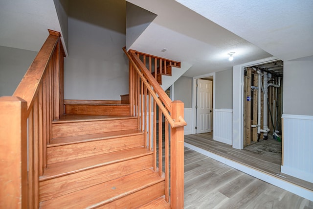 stairs featuring a textured ceiling, wood finished floors, and wainscoting