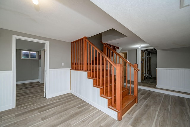 stairs featuring a wainscoted wall, a textured ceiling, and wood finished floors