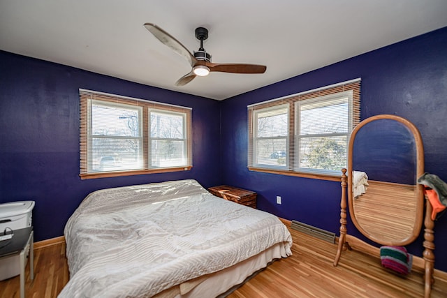 bedroom featuring multiple windows, a ceiling fan, baseboards, and wood finished floors