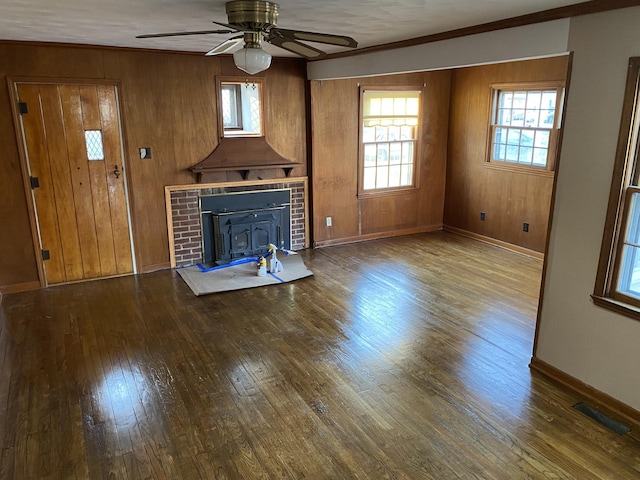 unfurnished living room featuring a ceiling fan, visible vents, baseboards, hardwood / wood-style flooring, and wood walls