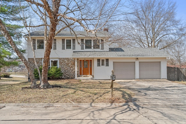 traditional home featuring stone siding, fence, concrete driveway, a garage, and a chimney