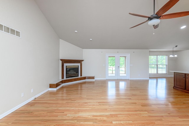 unfurnished living room featuring light wood finished floors, visible vents, baseboards, a glass covered fireplace, and high vaulted ceiling