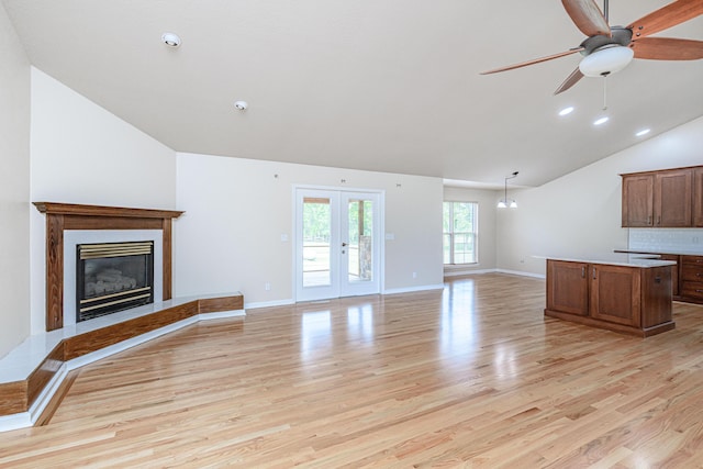 unfurnished living room with a glass covered fireplace, french doors, baseboards, light wood finished floors, and lofted ceiling