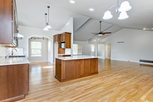 kitchen featuring brown cabinets, light countertops, stainless steel microwave, ceiling fan with notable chandelier, and open floor plan