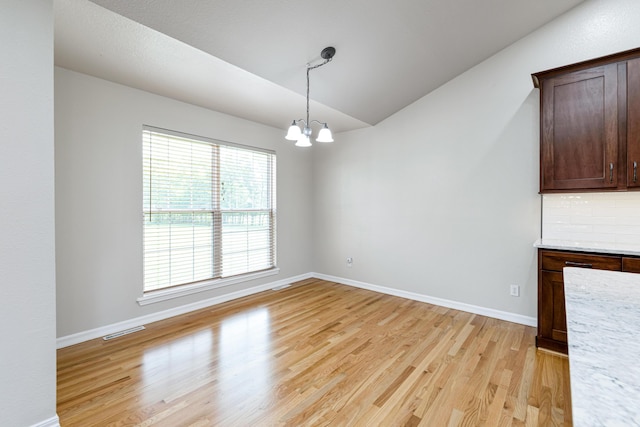 unfurnished dining area featuring visible vents, baseboards, light wood-type flooring, and lofted ceiling