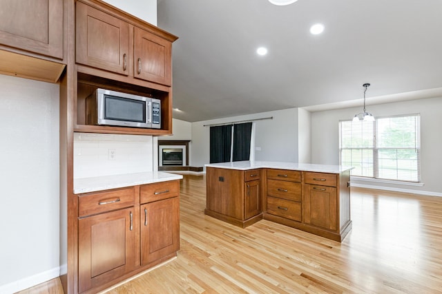 kitchen featuring stainless steel microwave, a center island, light wood-style floors, brown cabinetry, and light countertops