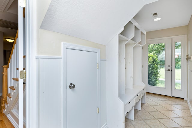 mudroom with visible vents, a wainscoted wall, lofted ceiling, light tile patterned flooring, and a textured ceiling