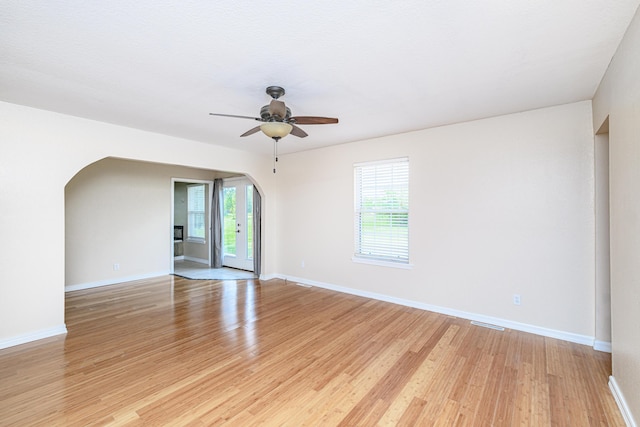 empty room featuring arched walkways, baseboards, a ceiling fan, and light wood-style floors