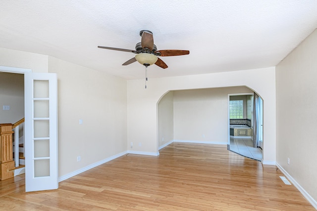 empty room featuring a ceiling fan, stairs, light wood-style floors, and arched walkways