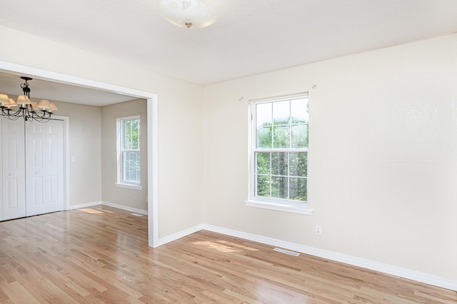 unfurnished room with visible vents, baseboards, an inviting chandelier, and light wood-style flooring