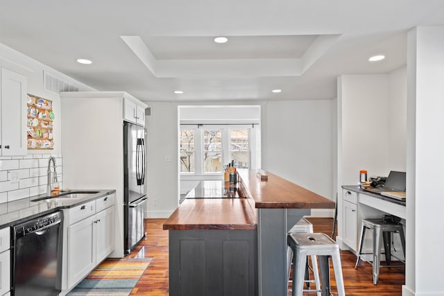 kitchen with butcher block counters, black appliances, a raised ceiling, and a sink